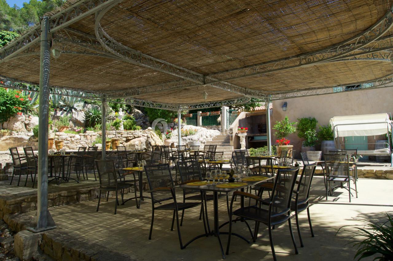 Terrasse ombragée avec tables et chaises en métal, entourée de végétation et de murs en pierre.