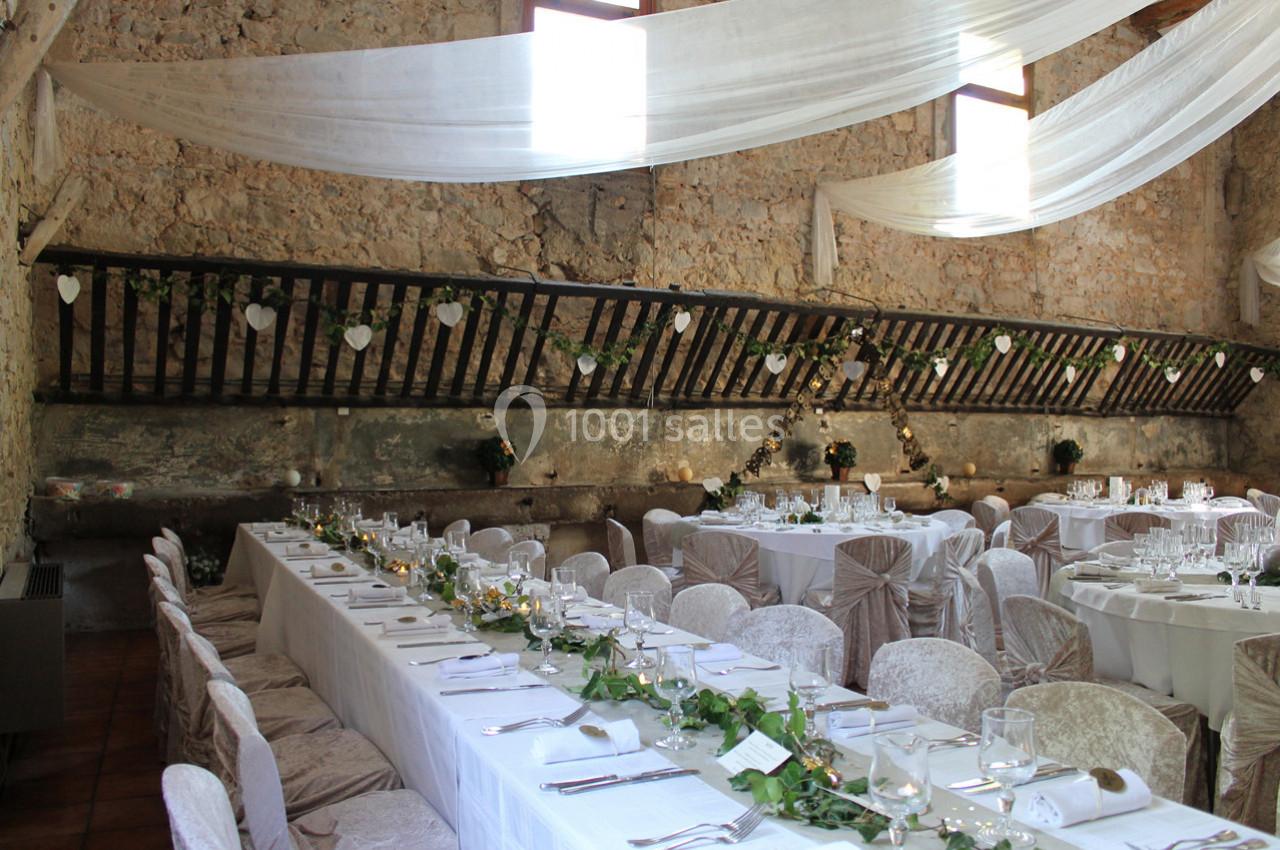 Salle de réception décorée pour un mariage, avec tables dressées, chaises couvertes et guirlandes végétales.