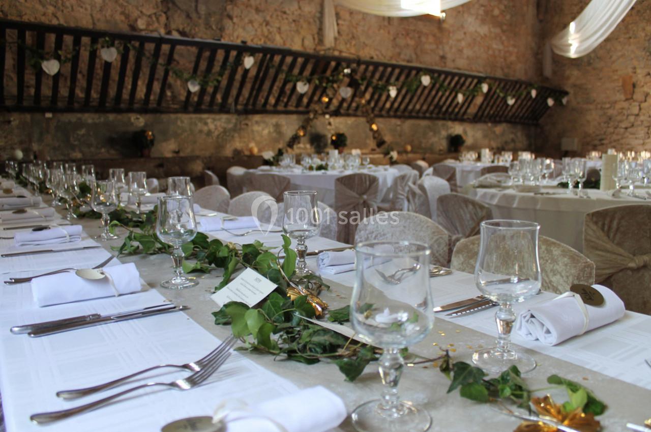 Salle de réception décorée pour un mariage avec longues tables dressées, nappes blanches et guirlandes de feuillage.
