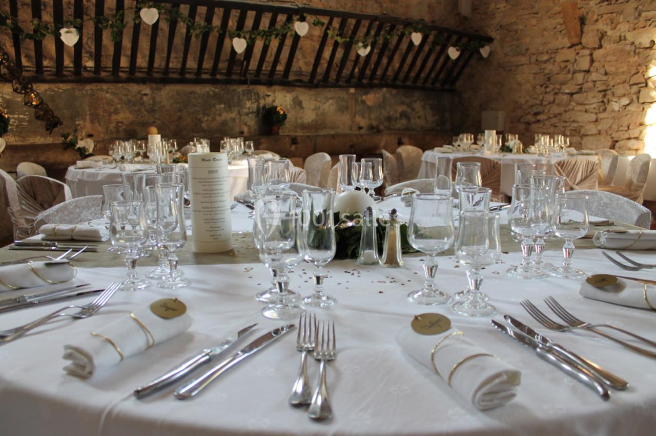 Tables élégamment dressées avec nappes blanches, verres et couverts dans une salle en pierre décorée pour un événement.