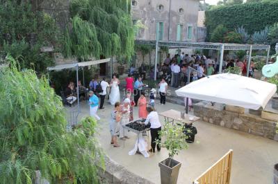 Groupe de personnes rassemblées dans une cour extérieure verdoyante devant un bâtiment en pierre avec des volets bleus.