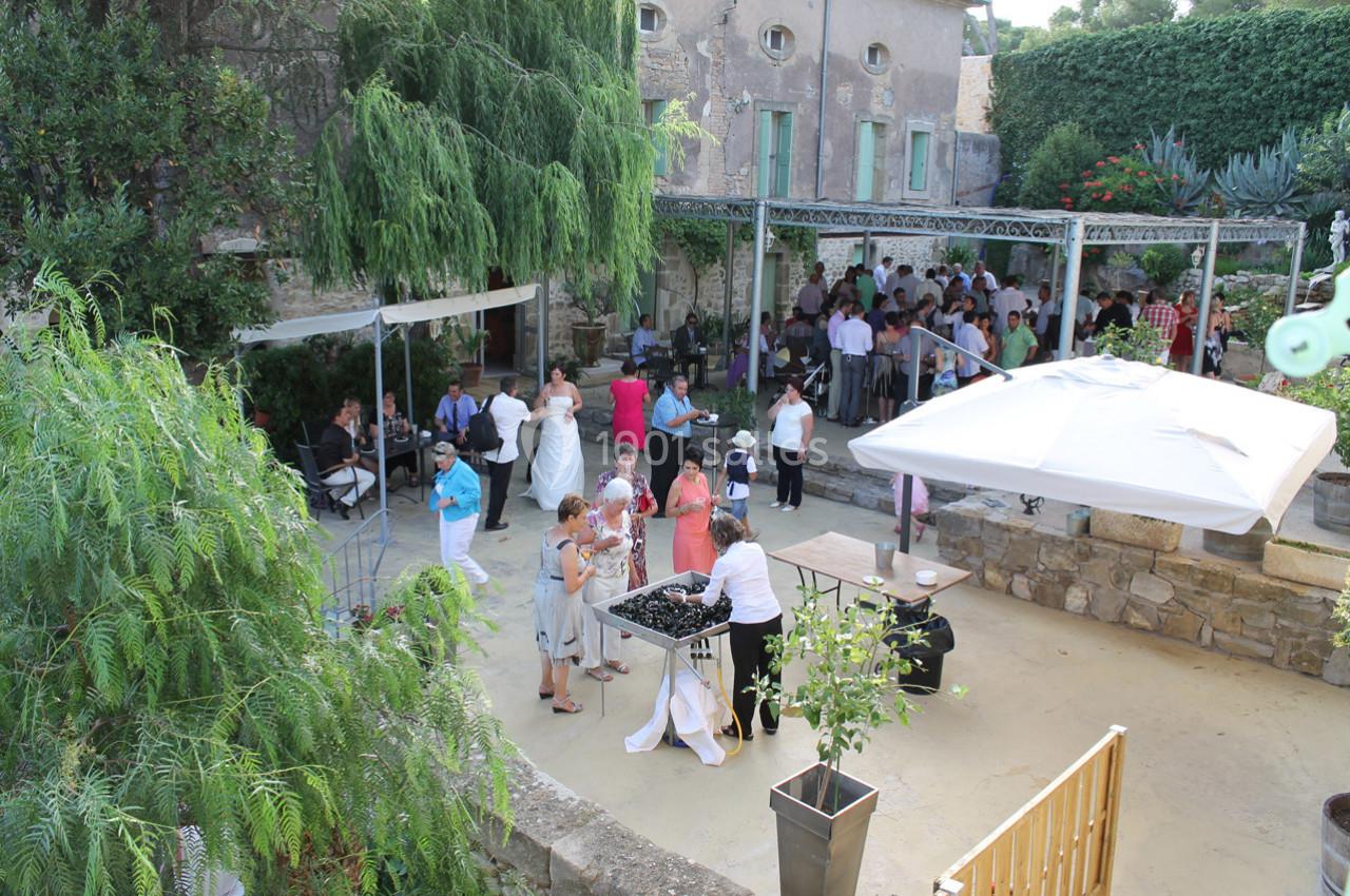 Groupe de personnes rassemblées dans une cour extérieure pour un événement, avec des tables et des arbres autour.