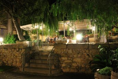 Groupe de personnes rassemblées dans une cour extérieure verdoyante devant un bâtiment en pierre avec des volets bleus.
