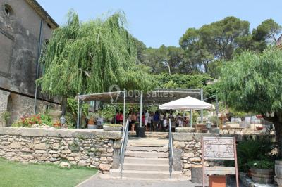 Groupe de personnes rassemblées dans une cour extérieure verdoyante devant un bâtiment en pierre avec des volets bleus.