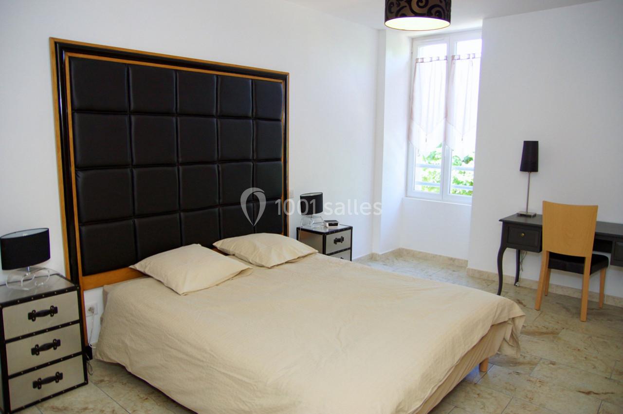 Chambre lumineuse avec lit double, tête de lit rembourrée, bureau en bois, lampes et fenêtre donnant sur l'extérieur.