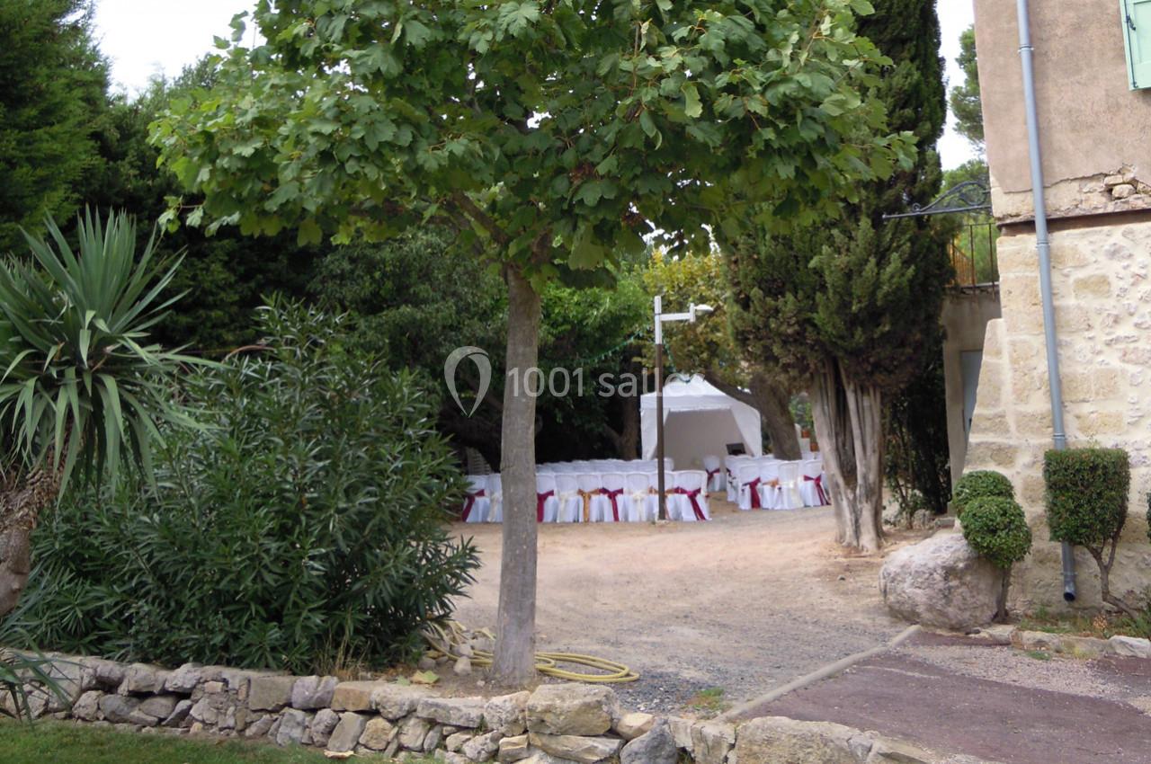 Chaises blanches décorées sous une tente dans un jardin arboré, près d'une maison en pierre.