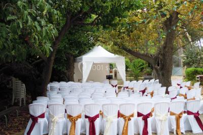 Groupe de personnes rassemblées dans une cour extérieure verdoyante devant un bâtiment en pierre avec des volets bleus.