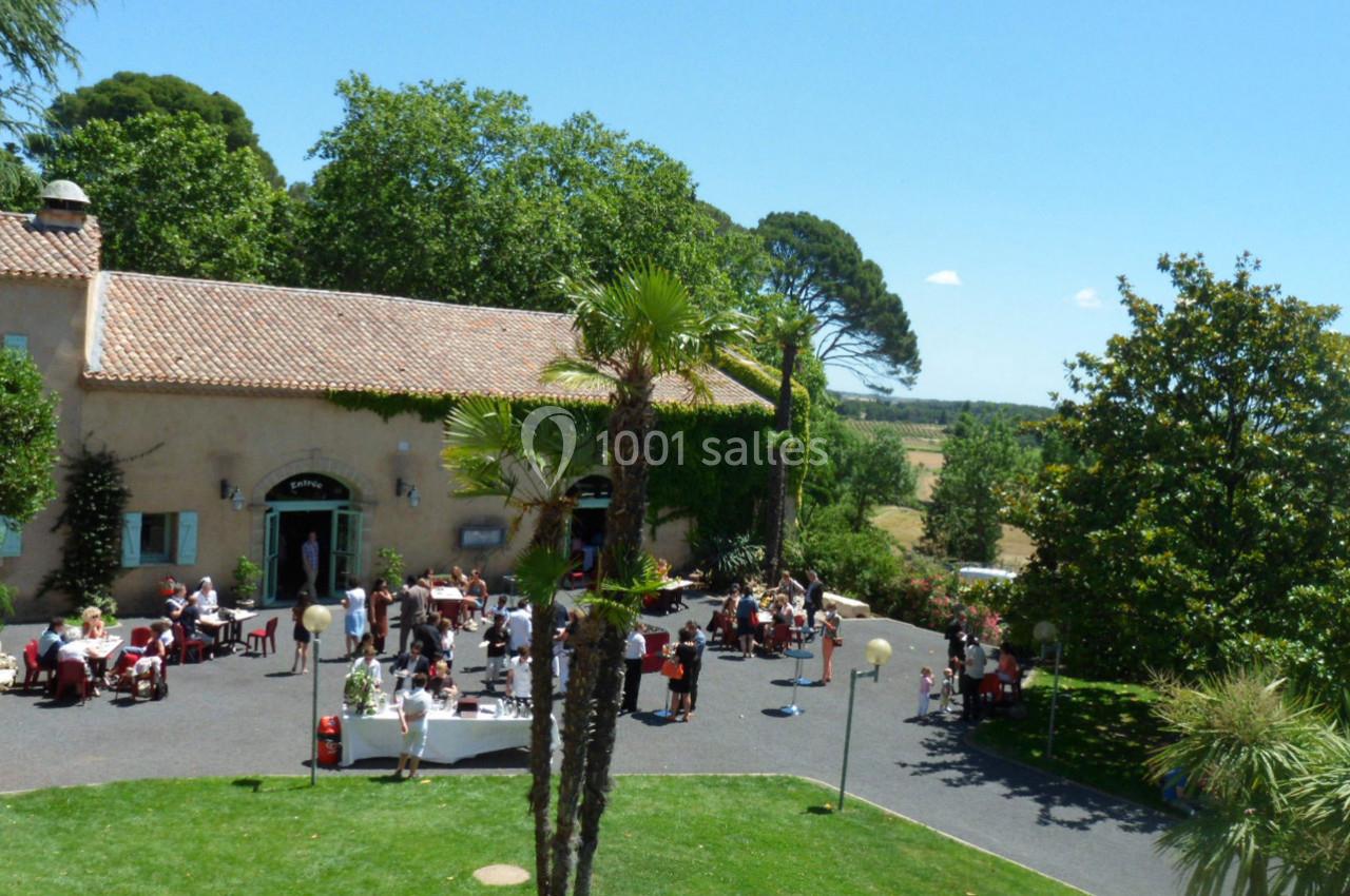 Personnes rassemblées dans la cour d'une grande maison en pierre entourée de verdure par une journée ensoleillée.