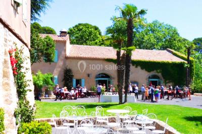 Groupe de personnes rassemblées dans une cour extérieure verdoyante devant un bâtiment en pierre avec des volets bleus.
