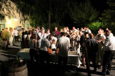 Groupe de personnes rassemblées dans une cour extérieure verdoyante devant un bâtiment en pierre avec des volets bleus.