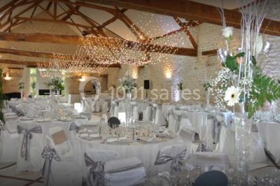 Salle de réception décorée avec des tables dressées, des guirlandes lumineuses et des arrangements floraux.