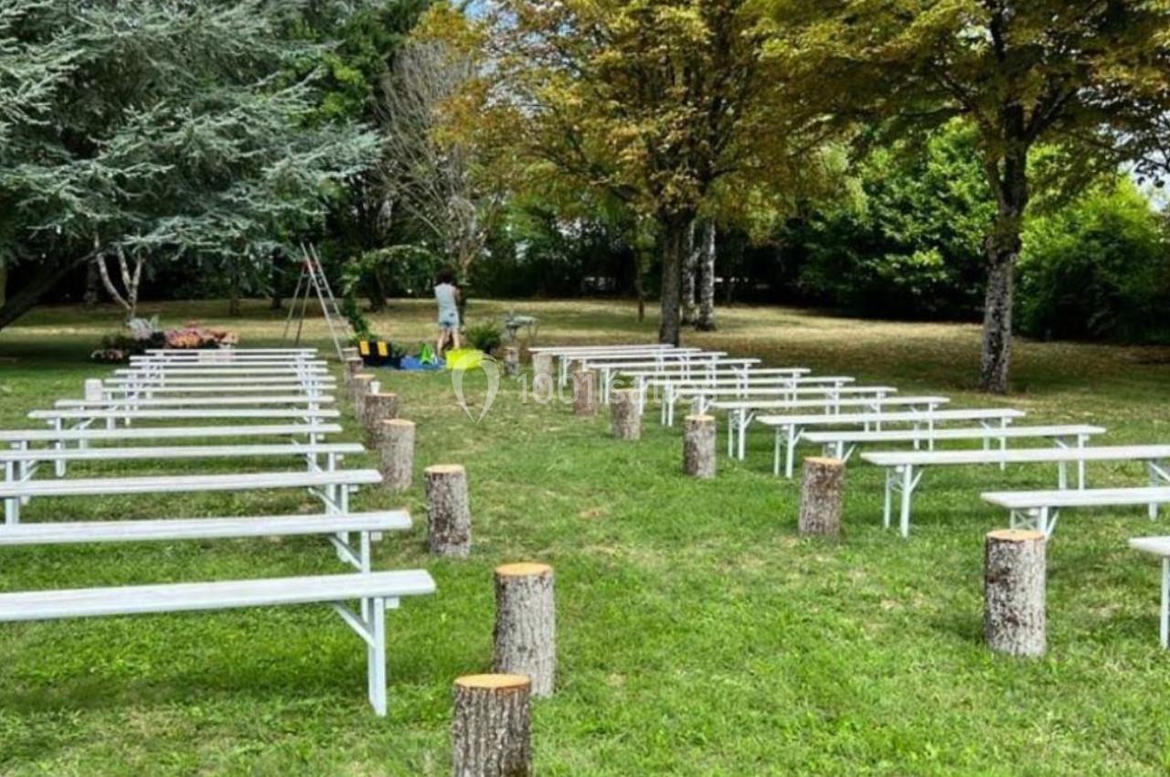 Bancs blancs alignés en extérieur sur une pelouse entourée d'arbres, avec des troncs d'arbres servant de décor.