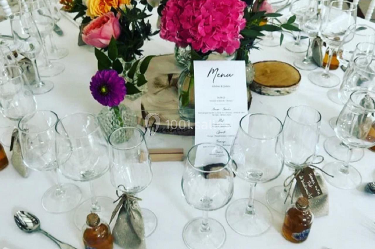 Table de réception décorée avec des fleurs colorées, des verres, des couverts, des menus et des petits cadeaux invités.