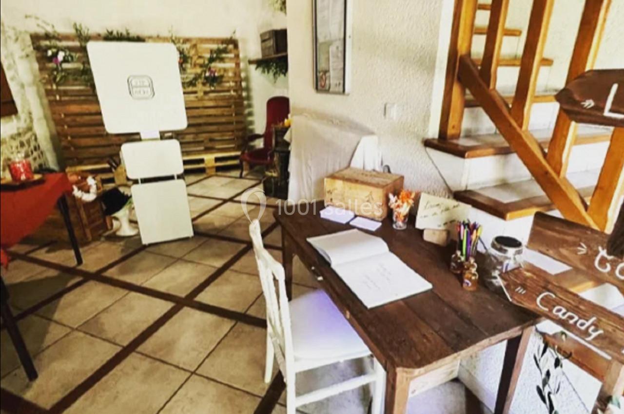 Coin aménagé avec une table en bois, des fournitures, un escalier en bois et un photobooth dans une pièce lumineuse.