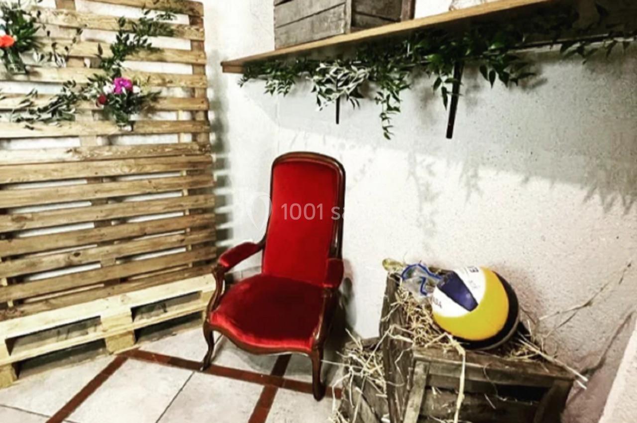 Chaise rouge ancienne dans un coin décoré avec des caisses en bois, des plantes et un ballon posé sur de la paille.