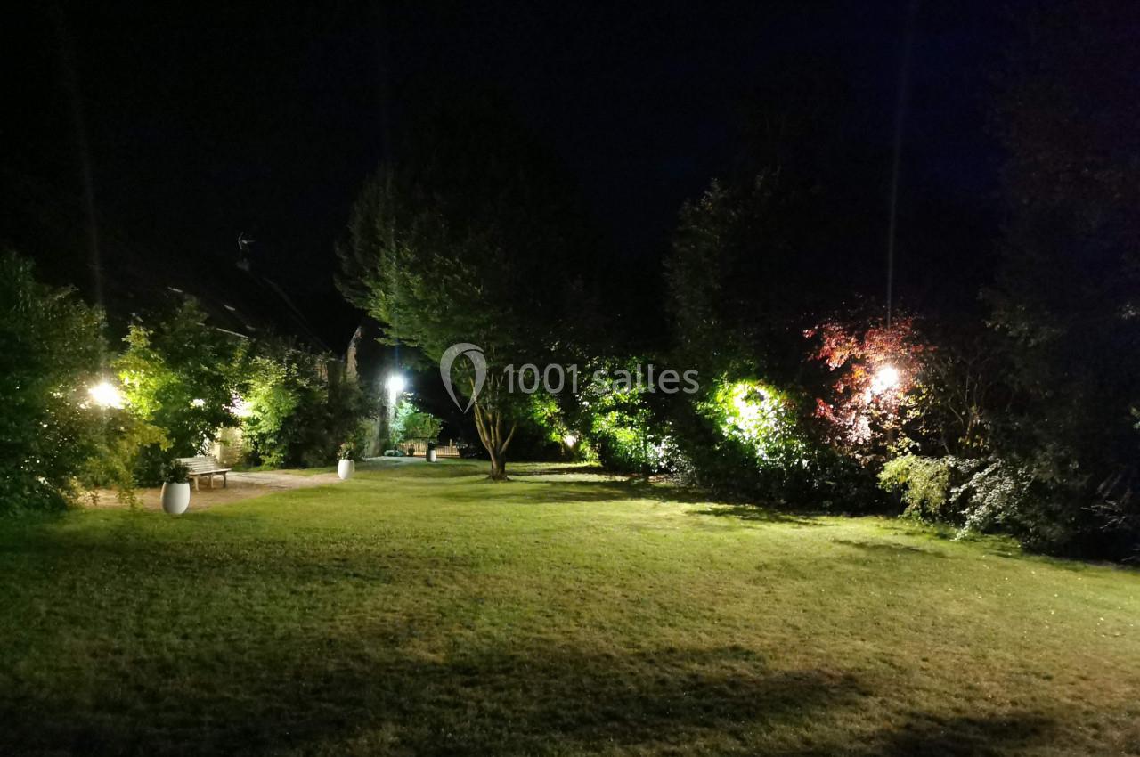 Pelouse éclairée la nuit avec des arbres et des buissons entourés de lumières tamisées.