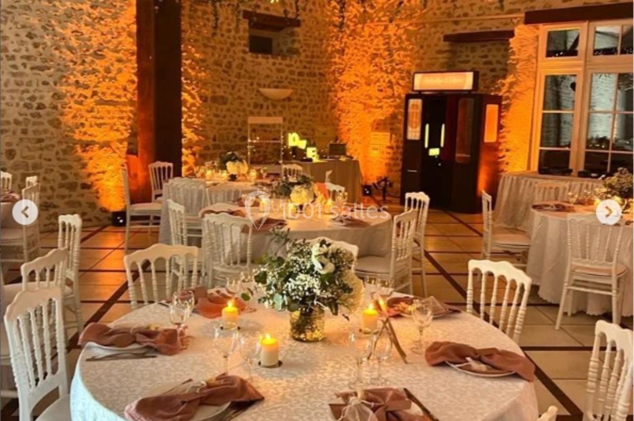Salle de réception décorée avec des tables rondes, nappes blanches, bougies et guirlandes lumineuses suspendues.