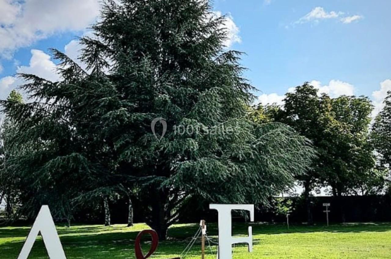 Lettres géantes ’A & F’ posées sur une pelouse verte, avec un grand arbre et un ciel bleu en arrière-plan.