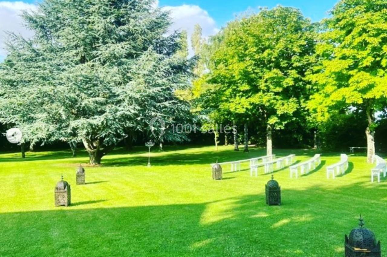 Pelouse verdoyante avec chaises blanches alignées pour un événement en plein air, entourée d'arbres et de lanternes…