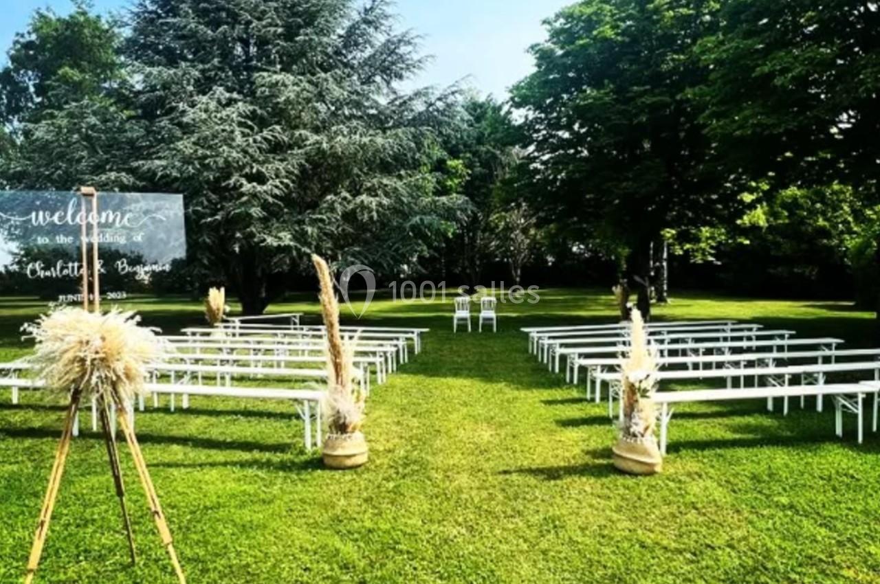 Chaises blanches alignées en extérieur sur une pelouse, entourées d'arbres, avec un panneau de bienvenue décoratif.