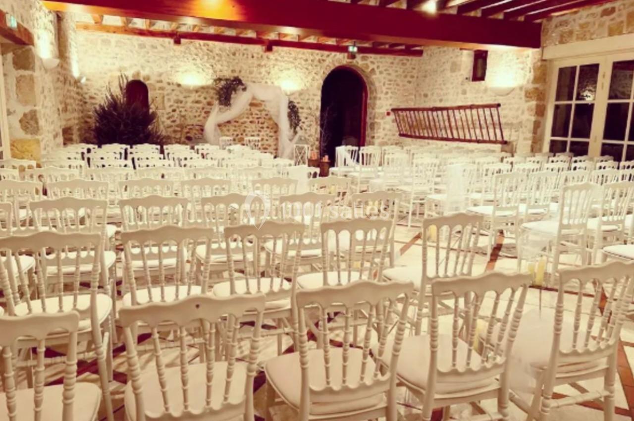 Salle de réception en pierre avec des chaises blanches alignées et une décoration légère en arrière-plan.