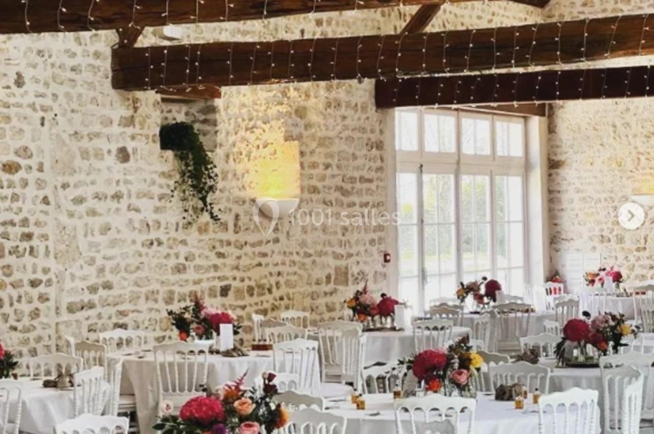 Salle de réception lumineuse avec murs en pierre, poutres apparentes et tables décorées de fleurs colorées.