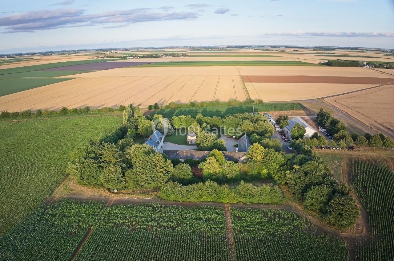 Vue aérienne d'une propriété entourée d'arbres au milieu de champs agricoles sous un ciel dégagé.