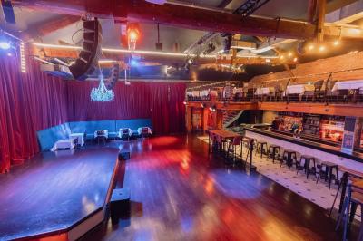 Salle avec un bar central, tabourets alignés, mezzanine avec tables, éclairage chaleureux et poutres apparentes.