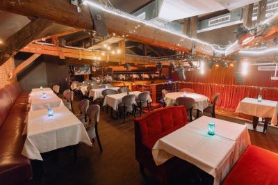 Salle avec un bar central, tabourets alignés, mezzanine avec tables, éclairage chaleureux et poutres apparentes.