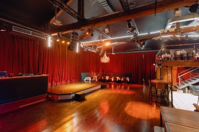 Salle avec un bar central, tabourets alignés, mezzanine avec tables, éclairage chaleureux et poutres apparentes.