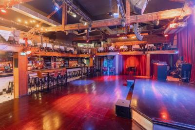 Salle avec un bar central, tabourets alignés, mezzanine avec tables, éclairage chaleureux et poutres apparentes.