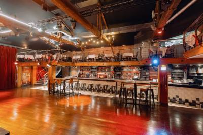 Salle avec un bar central, tabourets alignés, mezzanine avec tables, éclairage chaleureux et poutres apparentes.