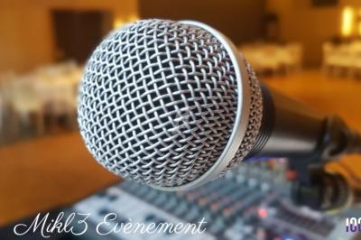 Gros plan sur un microphone devant une table de mixage dans une salle éclairée, avec des tables en arrière-plan flou.