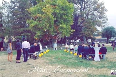 Cérémonie en plein air avec invités assis devant un arbre, décorée de lanternes jaunes et tables hautes blanches.