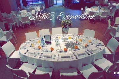 Salle de réception avec tables rondes dressées pour un événement, décorées de nappes blanches et d'un centre de table floral.