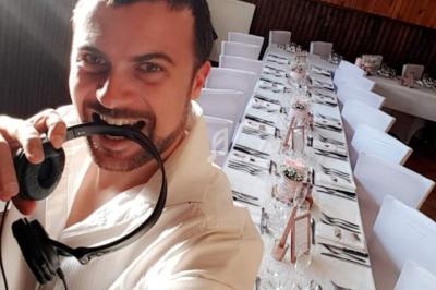 Un homme souriant tenant un casque audio, devant une table de réception décorée dans une salle lumineuse.