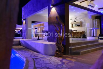 Un groupe de musiciens joue sur une petite scène extérieure sous un ciel bleu, entouré de décorations en bois.