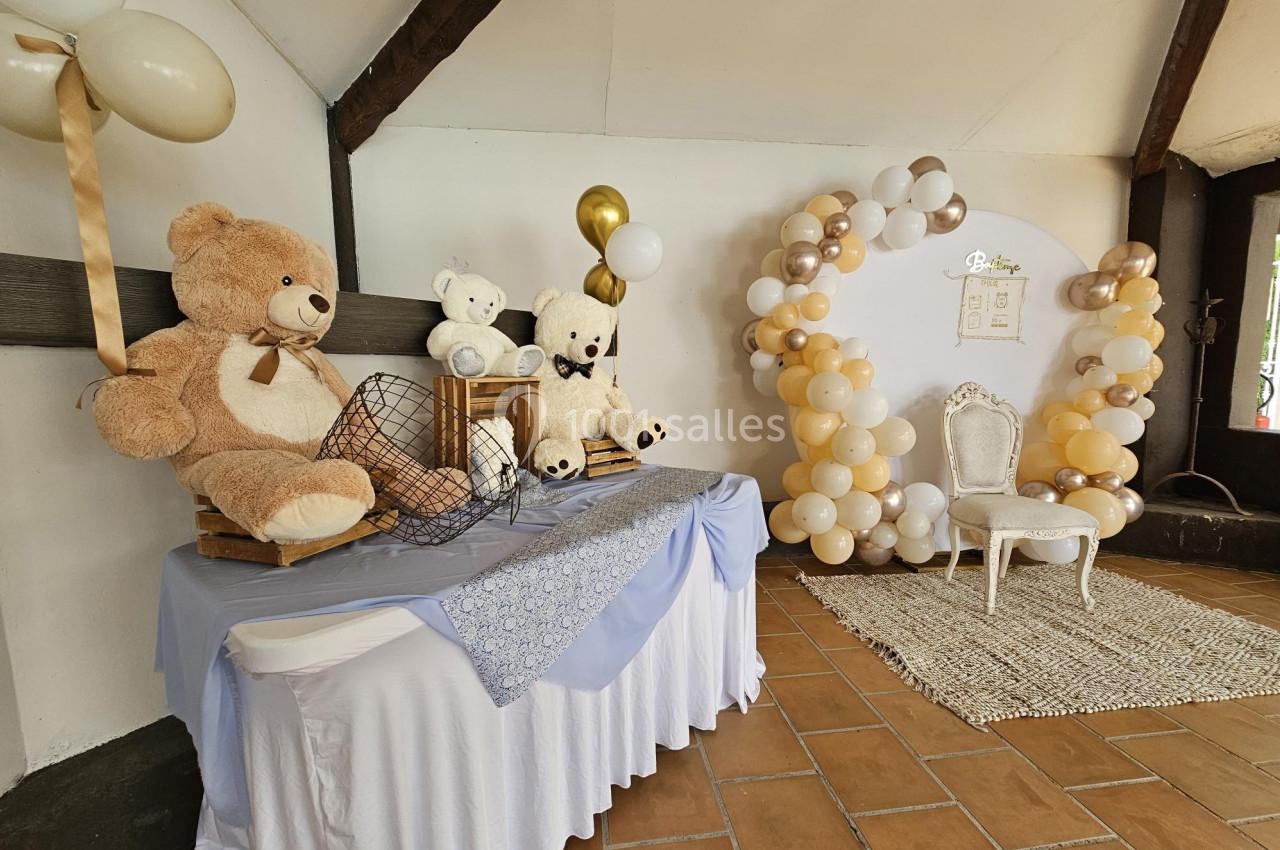 Décoration de fête avec des ballons beige et blanc, des ours en peluche et une chaise blanche sur un tapis.