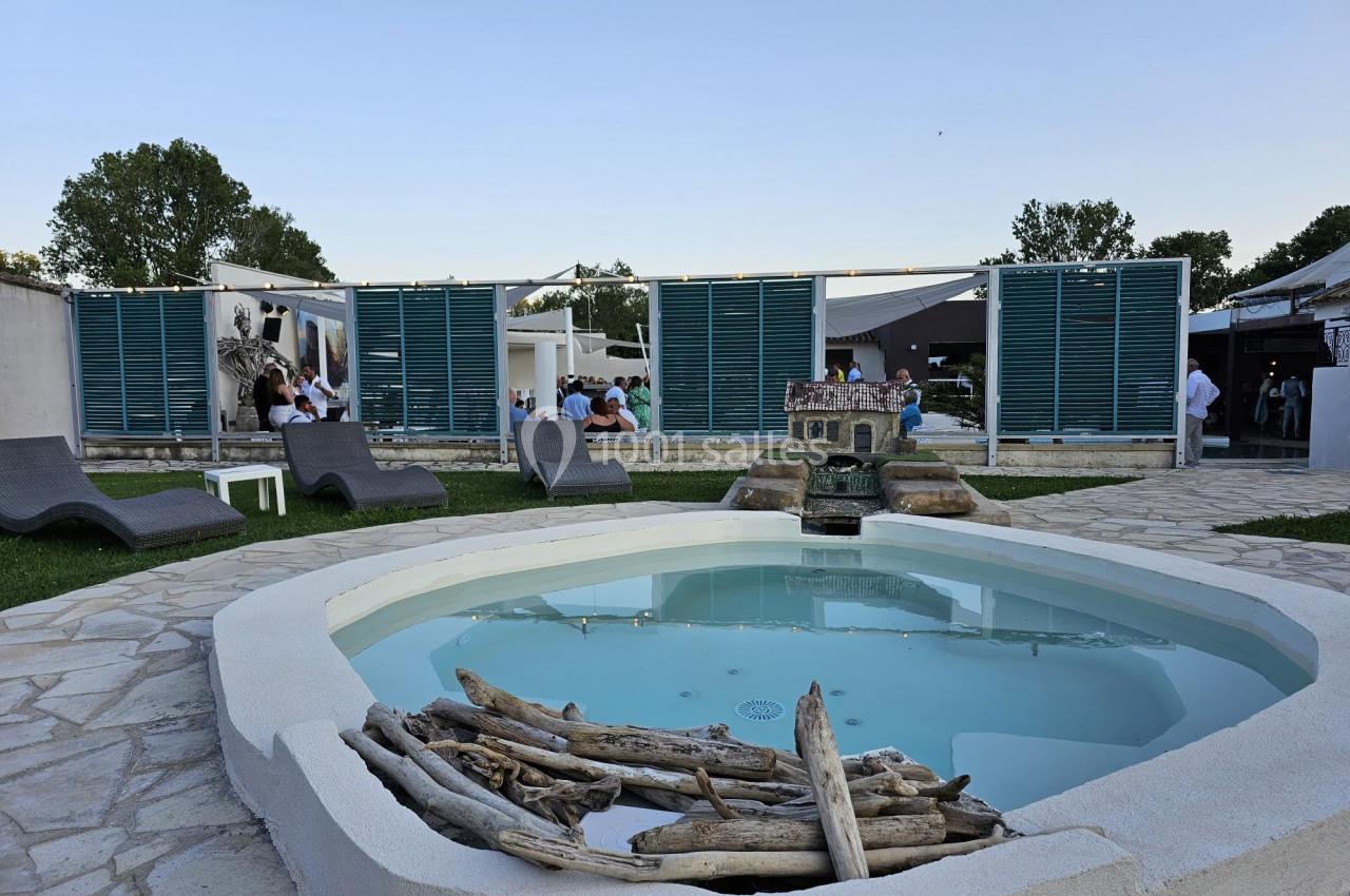Petit bassin rond entouré de pierres, avec des transats et des panneaux en bois devant un espace extérieur animé.