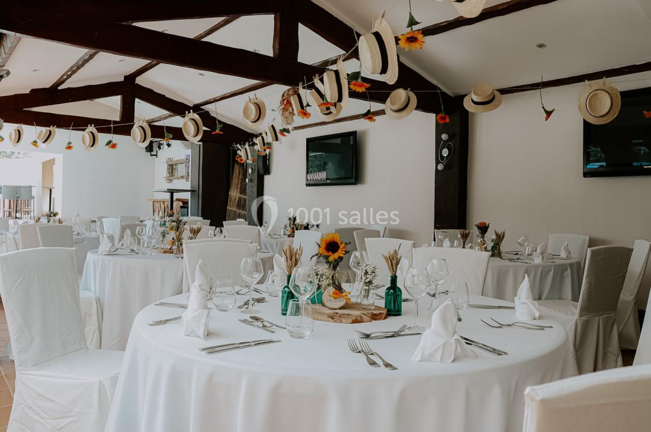 Salle de réception décorée avec des tables rondes dressées, des chapeaux suspendus et des touches de tournesols.