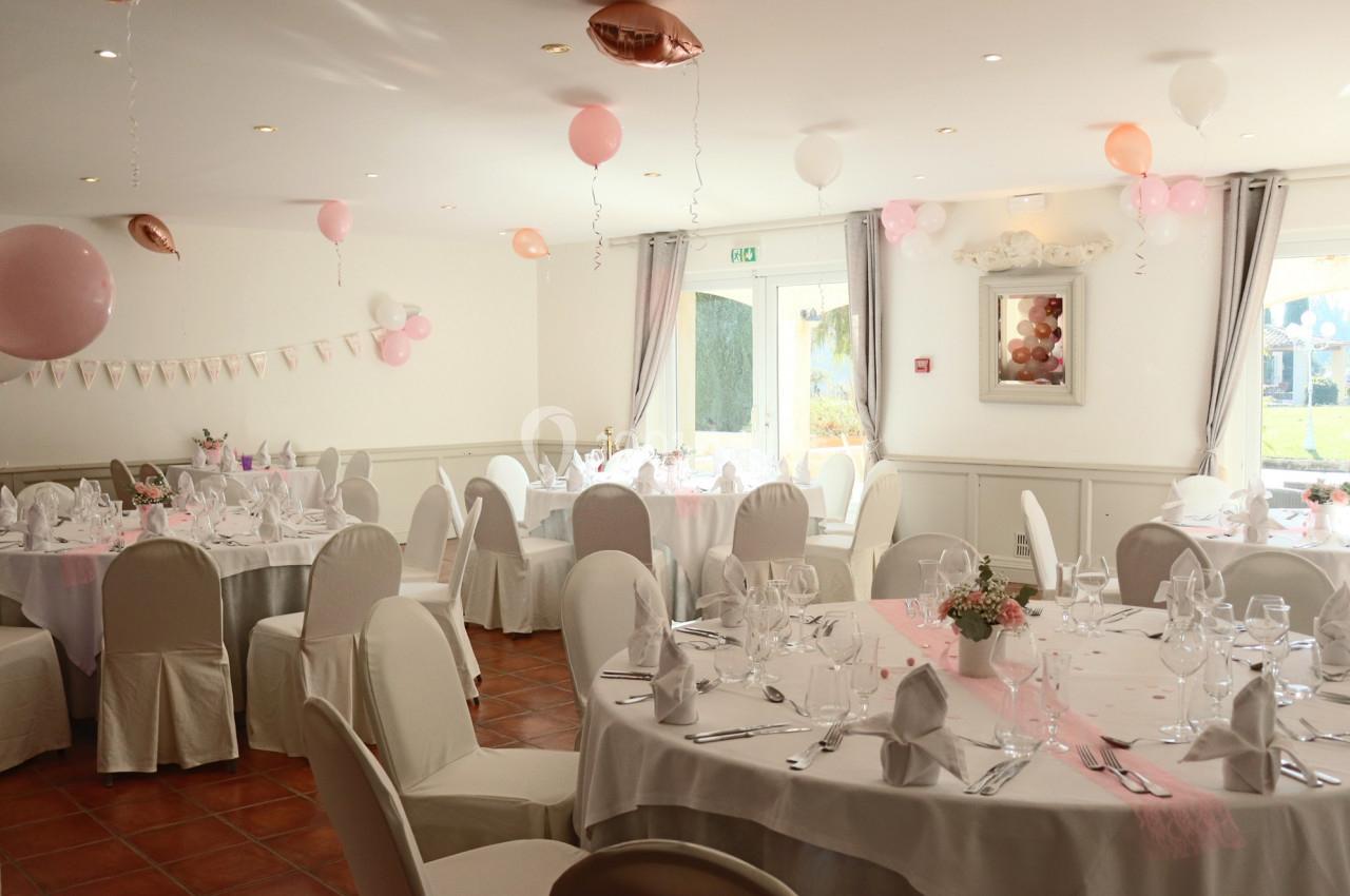 Salle de réception décorée avec des ballons roses et blancs, des nappes blanches et des tables dressées pour un événement.