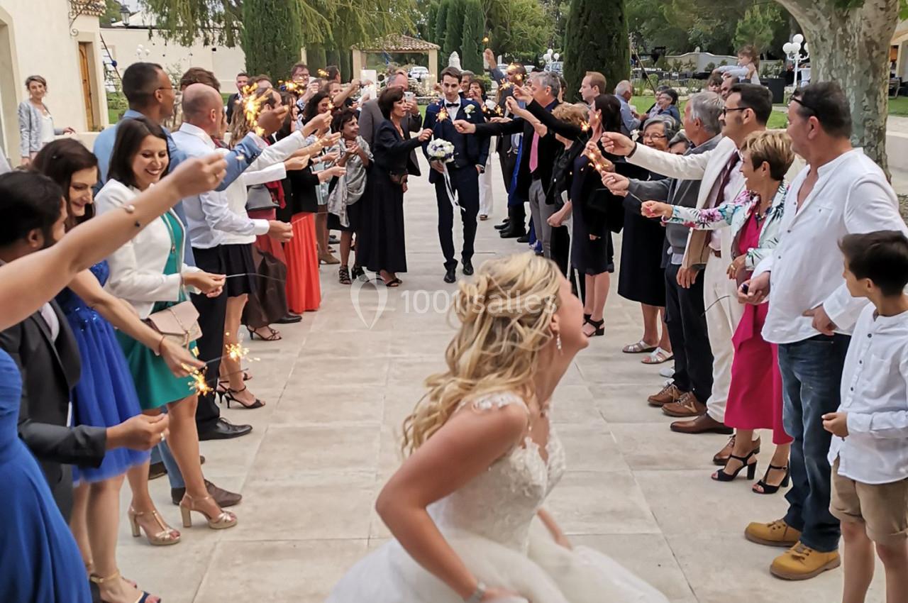 Une mariée court vers un groupe de personnes tenant des cierges magiques, formant une allée festive en extérieur.