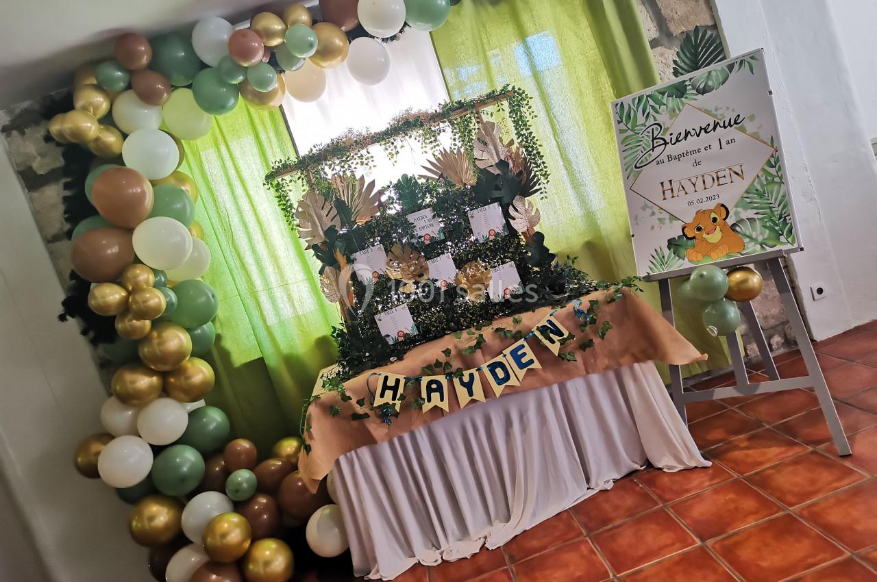 Décoration de fête avec ballons verts, blancs et dorés, table ornée de feuillages et panneau de bienvenue personnalisé.