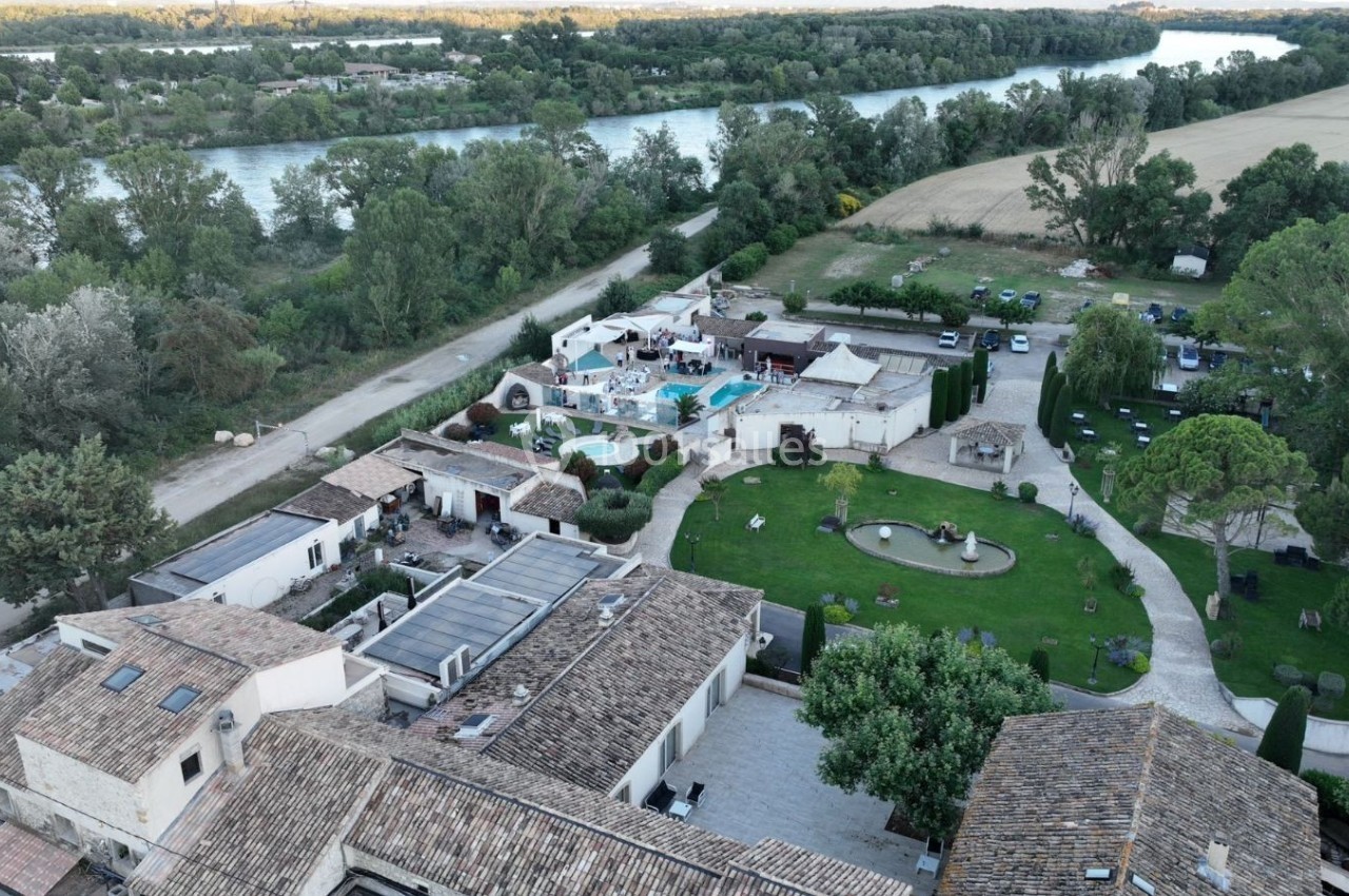 Vue aérienne d'un domaine avec bâtiments en pierre, piscine, jardins aménagés et rivière en arrière-plan.