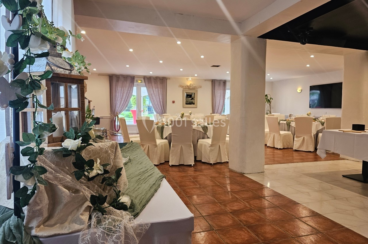 Salle de réception décorée avec des fleurs blanches, des nappes élégantes et des chaises habillées, éclairée par des spots.
