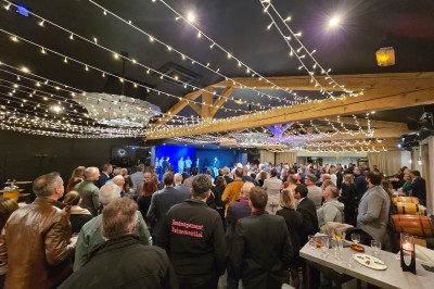 Un groupe de musiciens joue sur une petite scène extérieure sous un ciel bleu, entouré de décorations en bois.