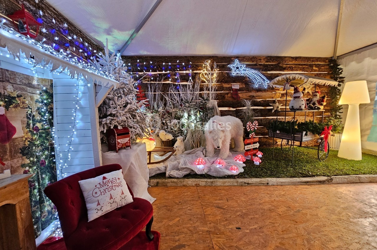 Décoration de Noël avec sapins enneigés, ours polaire factice, guirlandes lumineuses et fauteuil rouge dans un espace…