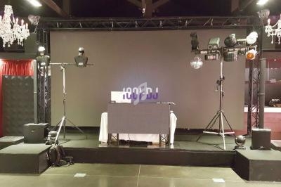 Installation de matériel de sonorisation et d'éclairage sur une scène avec écran et chandeliers suspendus.