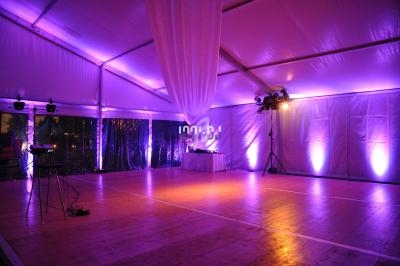 Intérieur d'une tente événementielle éclairée en violet, avec piste de danse en bois et table décorative au fond.