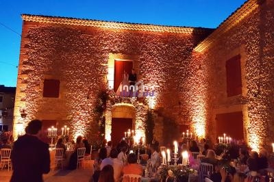 Façade en pierre éclairée par des lumières chaudes lors d'une réception en soirée avec des invités assis à table.